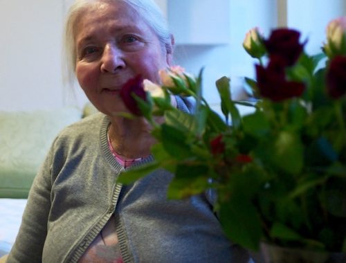 Fotograf: Henry Bronett. Porträtt, foto av Karla Bronett sittandes i bekväm fåtölj bakom en bukett rosor.