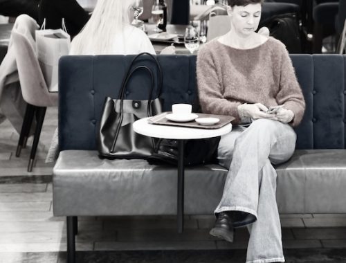 Streetphoto av Henry Bronett. Kvinna på kafé skrollar i mobiltelefon.